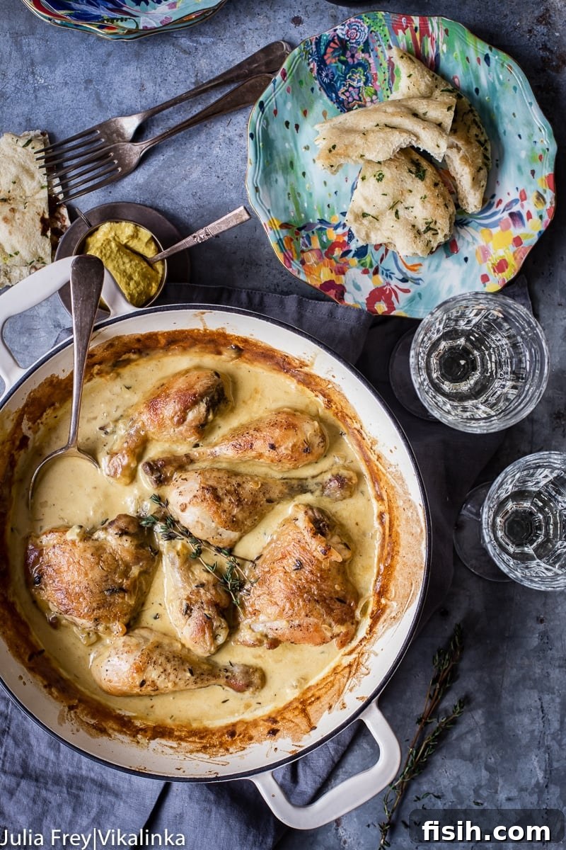 Creamy Wine Mustard Chicken 6 A white pan filled with chicken in creamy sauce, accompanied by two wine glasses and a plate of crusty torn bread, set for a delightful meal.