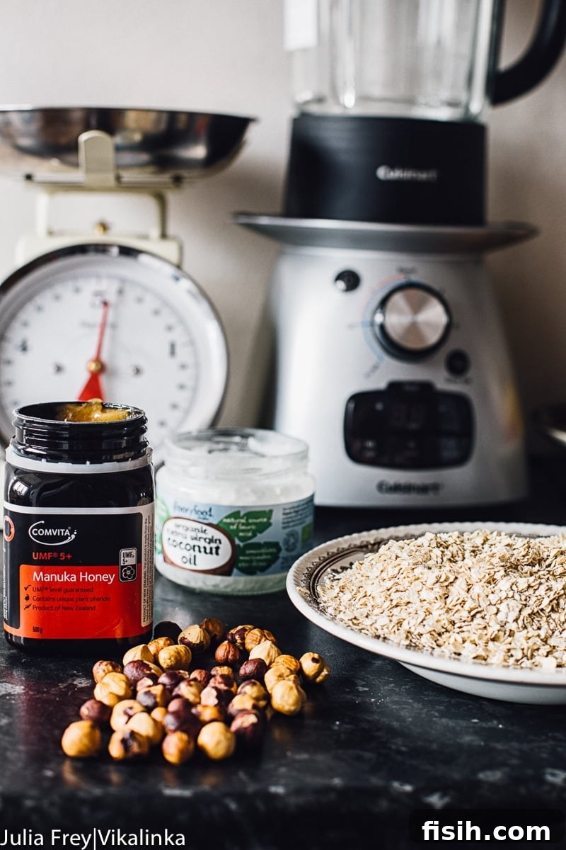 A selection of raw ingredients, including oats, hazelnuts, and Manuka honey, neatly arranged on a granite countertop, ready for baking homemade granola bars.