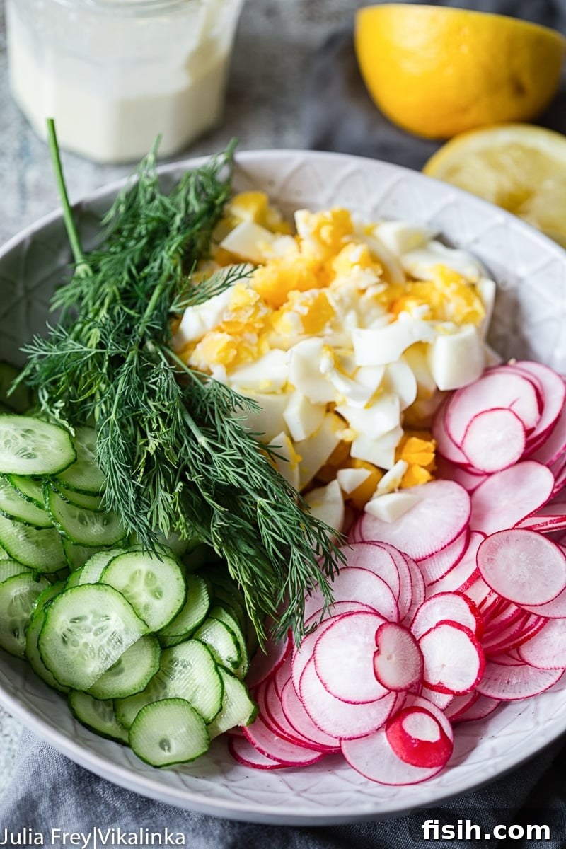 Close-up of thinly sliced cucumbers, radishes, and chopped hard-boiled eggs with fresh dill in a bowl, ready for dressing.
