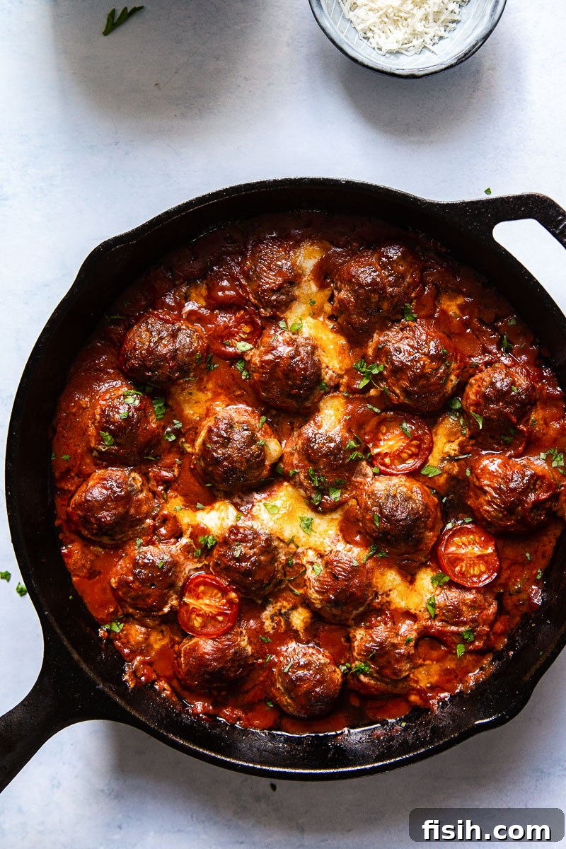 Rich tomato and pesto sauce bubbling around baked meatballs