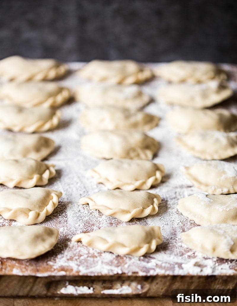 Smoky Bacon and Sweet Onion Potato Pierogi 5 Numerous uncooked Vareniki laid out neatly on a floured wooden board, showcasing their handcrafted perfection.