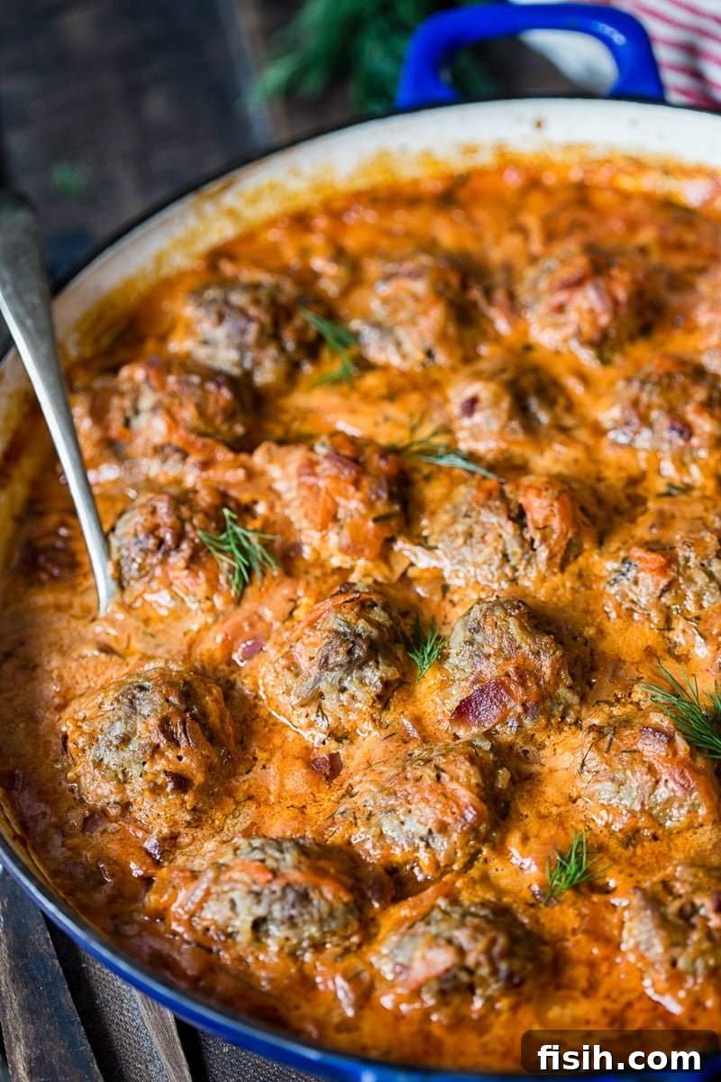 Delicious Porcupine Meatballs simmering in a rich tomato and sour cream sauce in a large pan, ready to be served.