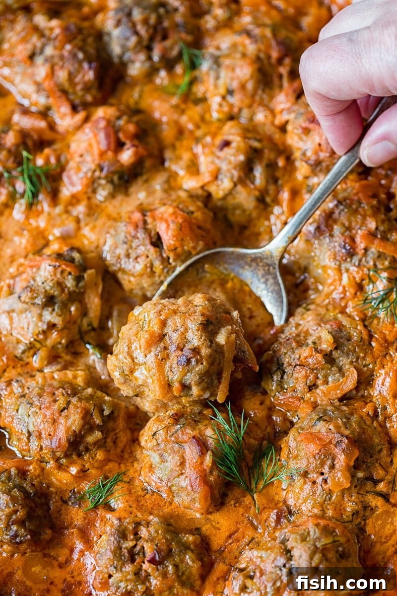 Close-up of baked Porcupine Meatballs in a rich, creamy tomato sauce, garnished with fresh dill.