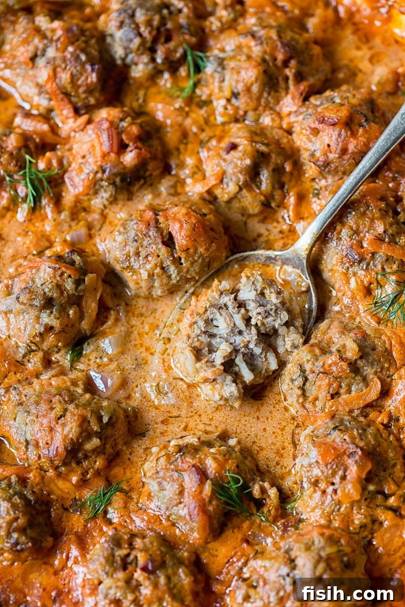 Close-up of a porcupine meatball on a spoon, showcasing its texture and the rich sauce.