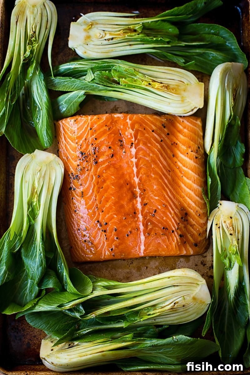 Close-up of baked salmon teriyaki alongside tender bok choy on a baking sheet.
