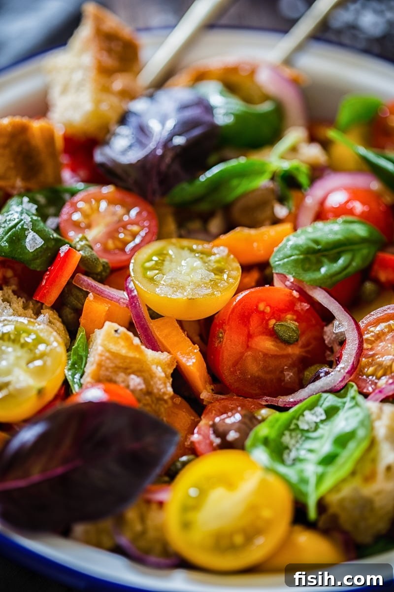 Rustic Tuscan Bread Salad 7 A close-up of a colorful Panzanella salad featuring red and yellow tomatoes, green and purple basil leaves, and crusty bread.