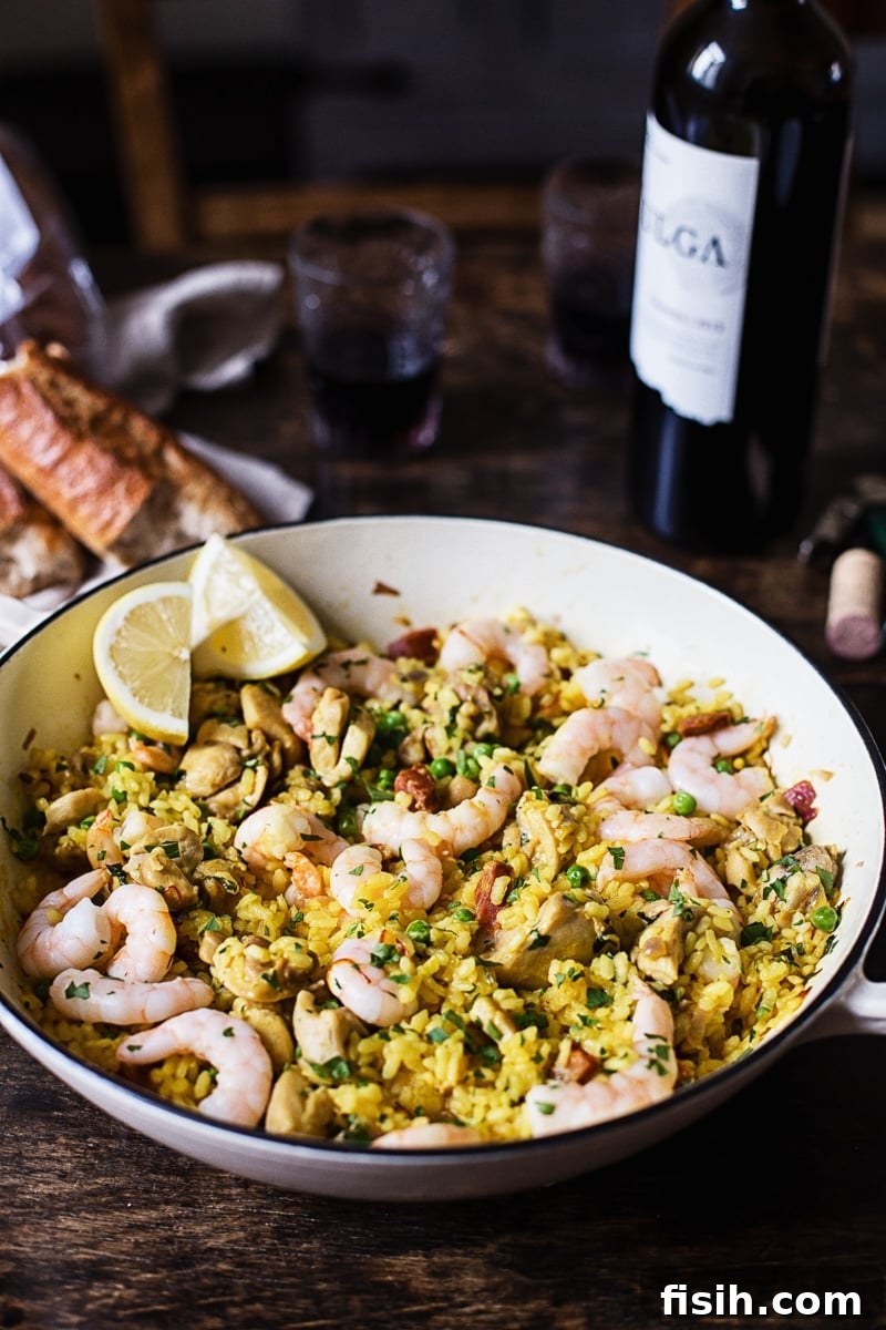 Spanish rice with shrimp in a while pan, baguette and wine in the background