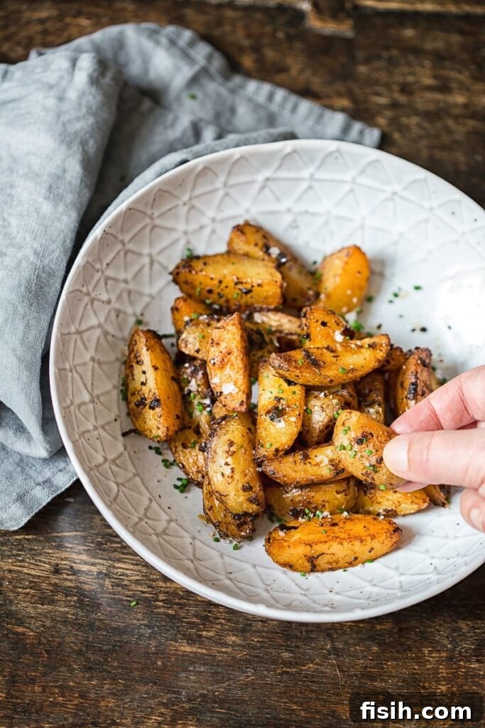 Hand grabbing a perfectly roasted chipotle mayo potato wedge from a rustic bowl, highlighting its crispy texture and golden-brown color.