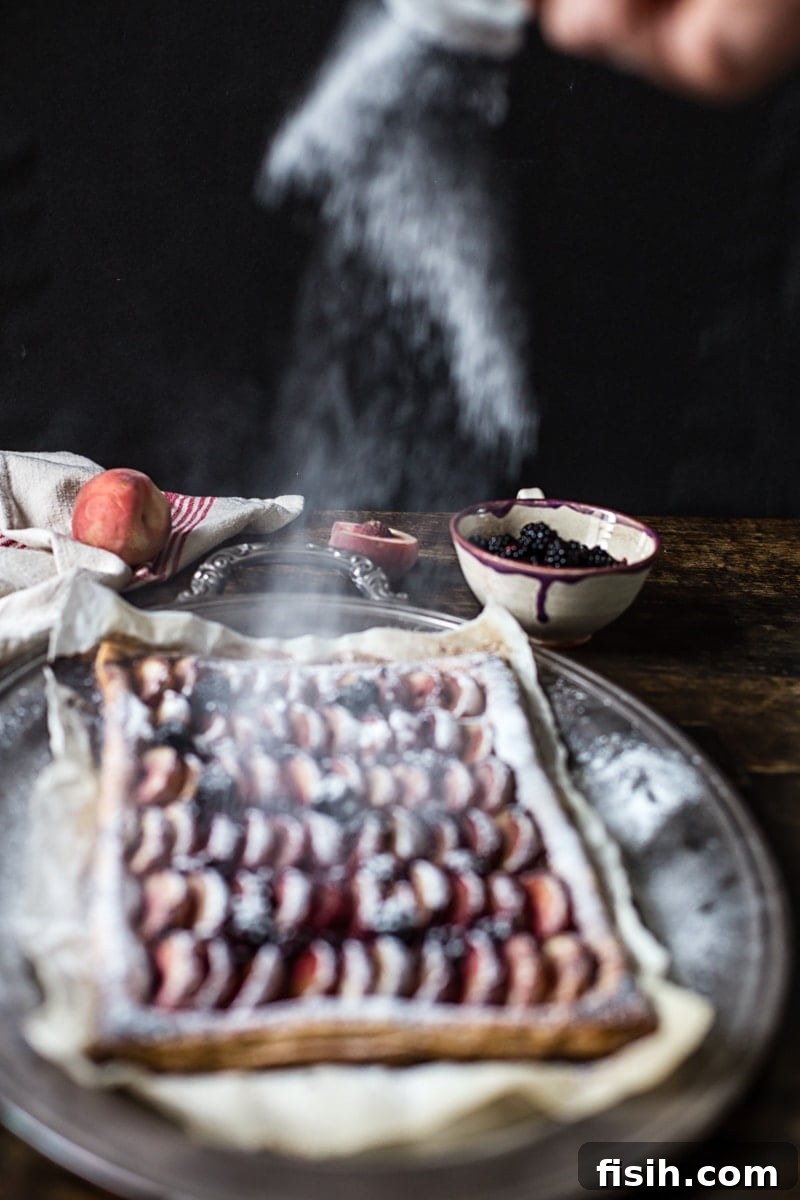 Icing sugar being sprinkled on the peach and blackberry tart