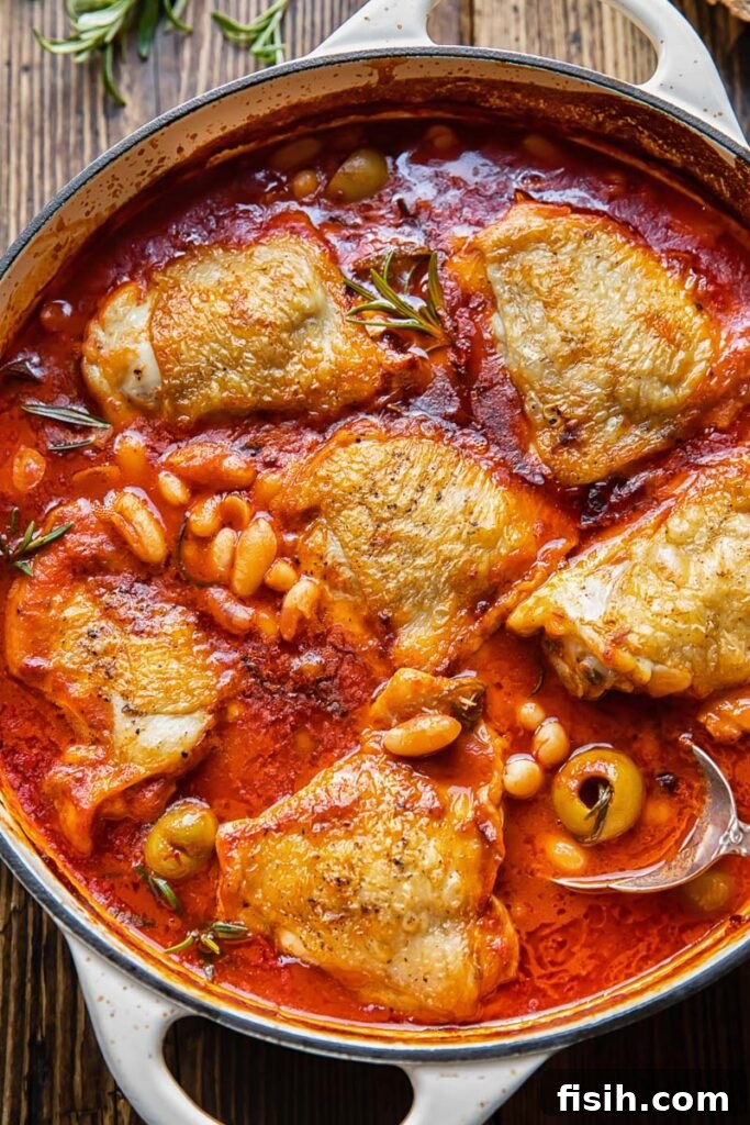 Top down view of Italian rosemary chicken stew in a pan, rich with tomato sauce, white beans, and olives.
