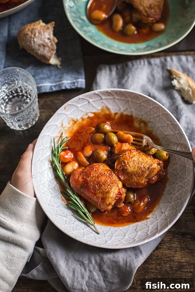 A hand holding a bowl of warm Italian Rosemary Chicken Stew, showing its rich texture and inviting steam.