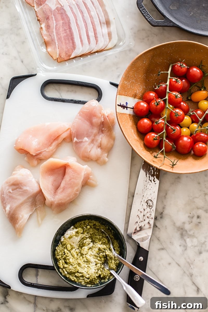 Ingredients for the recipe on a table, including pesto, tomatoes, chicken and proscuitto