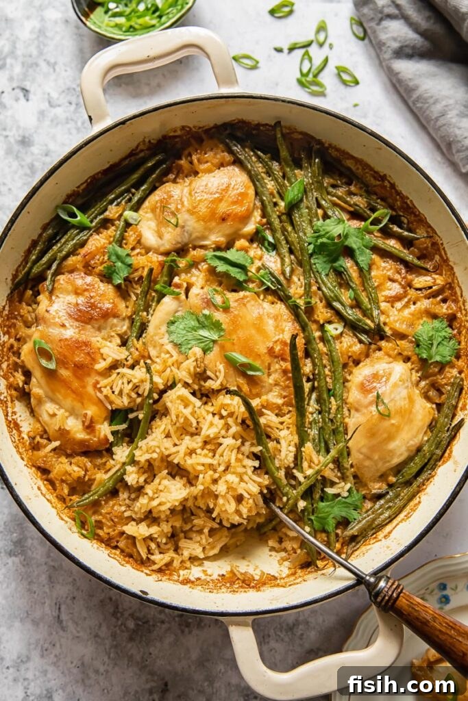 Overhead view of a white pan filled with Indonesian coconut chicken and rice, garnished with fresh herbs and surrounded by green beans.