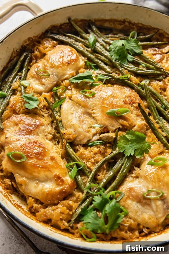 A close-up, top-down view of the finished coconut chicken and rice meal, garnished with fresh herbs, in a white pan.