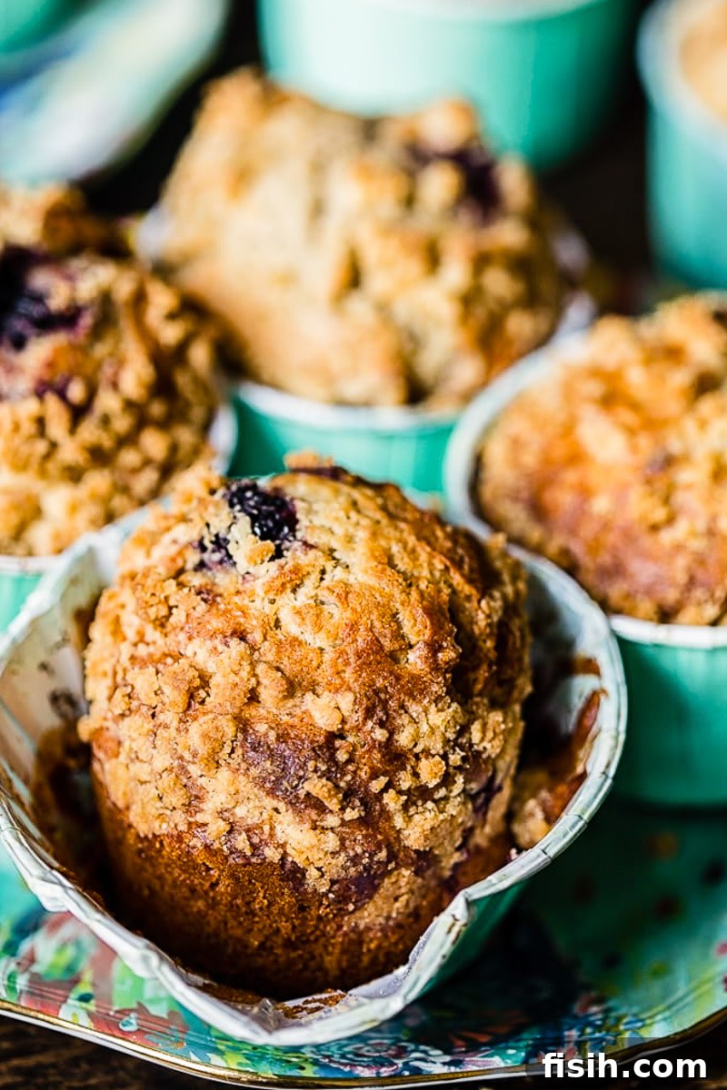 Gourmet Blackberry Burst Muffins 2 Close-up of a golden-brown bakery-style blackberry muffin with a crumble streusel topping and glistening, jammy blackberries peaking through, ready to be enjoyed.
