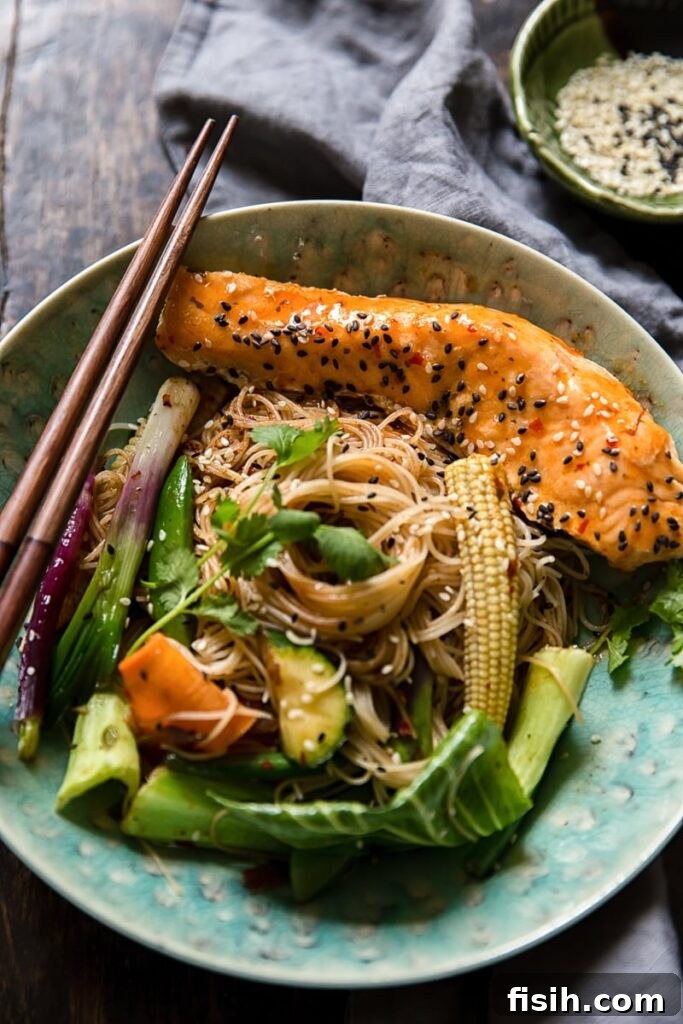 A delicious bowl of Chilli Salmon Mee Goreng, featuring stir-fried rice noodles, vibrant vegetables, and perfectly cooked salmon fillets, garnished with fresh herbs and sesame seeds.