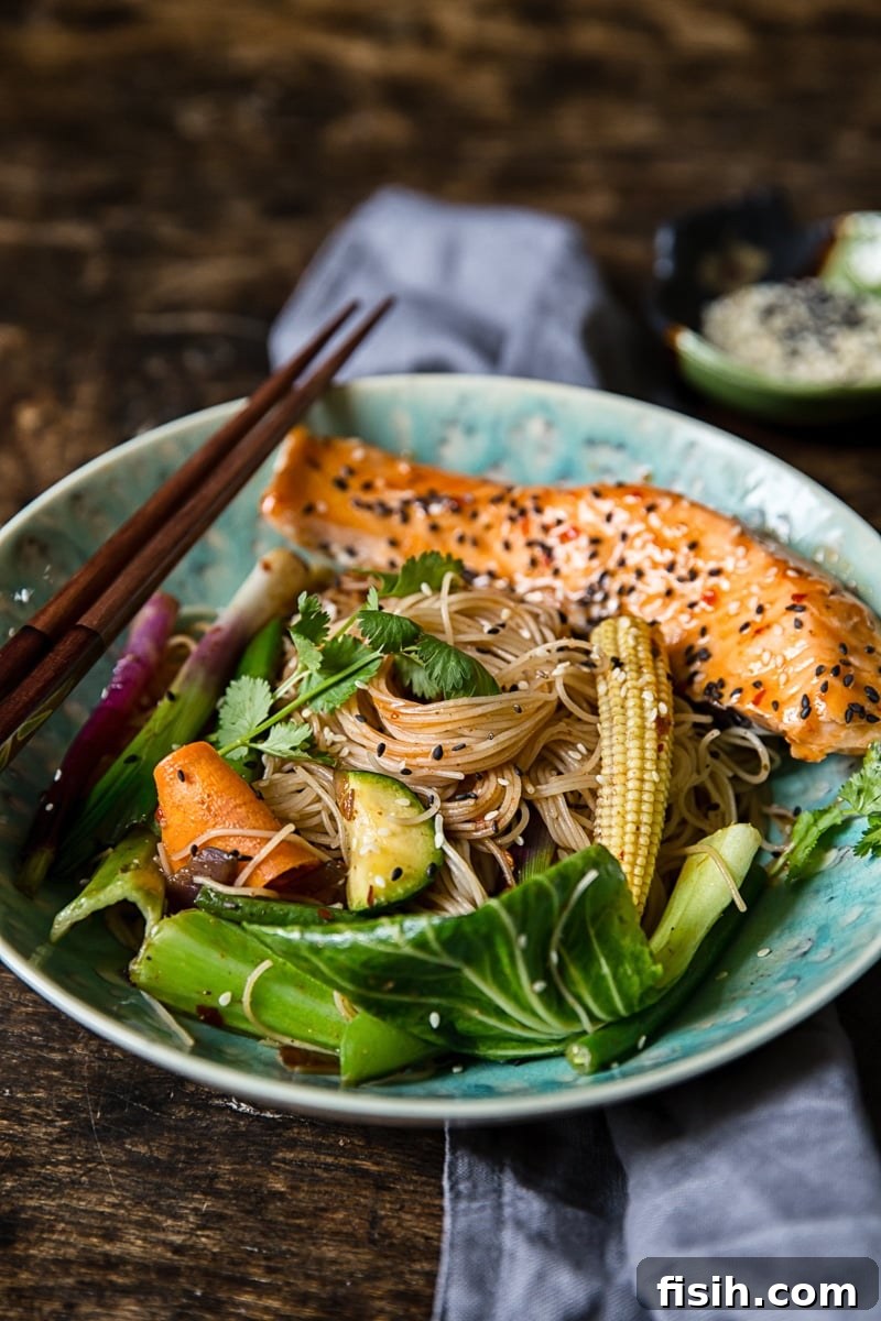 A close-up shot of Chilli Salmon Mee Goreng in a bowl, with chopsticks poised to pick up the flavorful noodles and salmon.