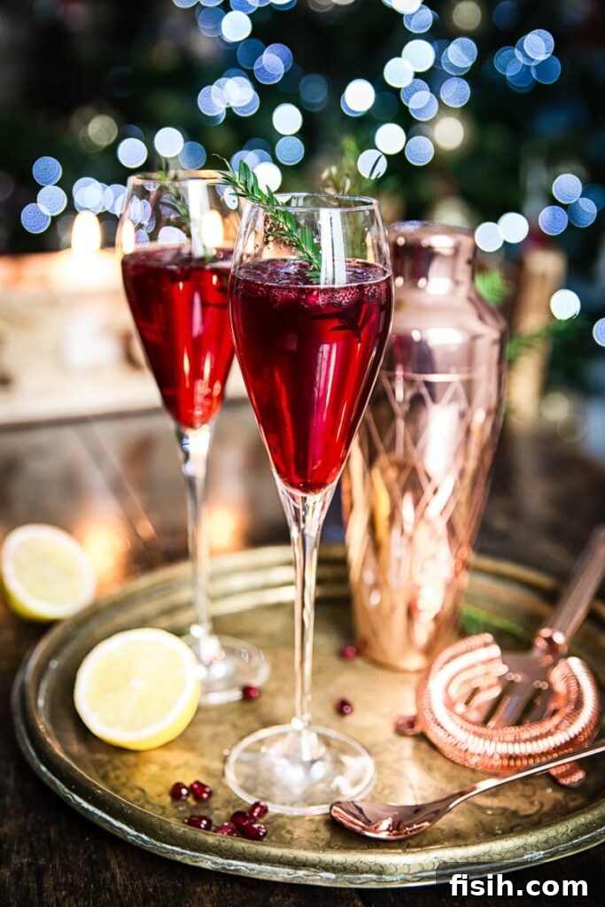 Two elegant glasses of Pomegranate French 75, garnished with pomegranate seeds and a sprig of pine, sitting on a festive platter