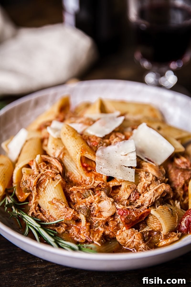 Braised Venetian Chicken Ragu Pasta 5 A close-up of a bowl of chicken ragu pasta, adorned with abundant, large shavings of Parmesan cheese, highlighting its rich texture.