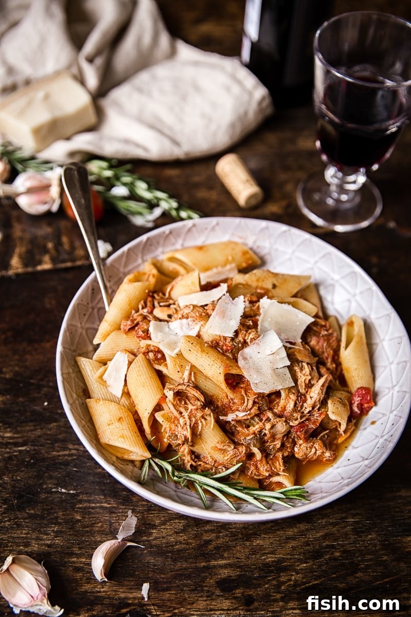 Braised Venetian Chicken Ragu Pasta 7 A beautiful bowl of chicken ragu pasta placed on a rustic wooden table, accompanied by a glass of red wine, creating a cozy dining scene.