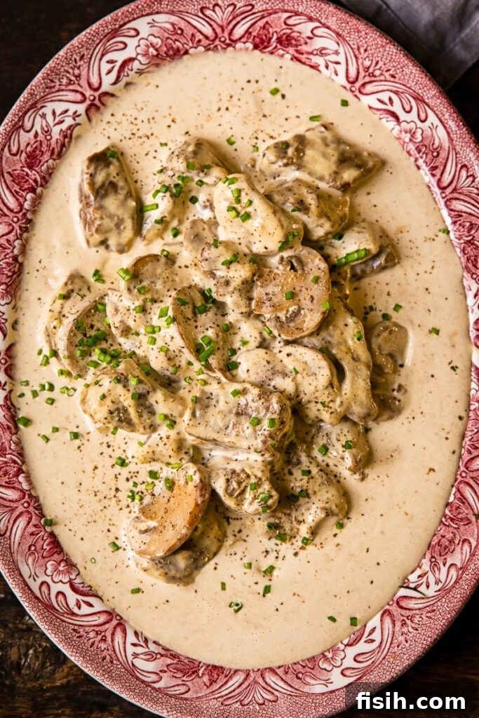 Close up of a plate with beef in creamy truffled mushroom sauce, garnished with fresh herbs