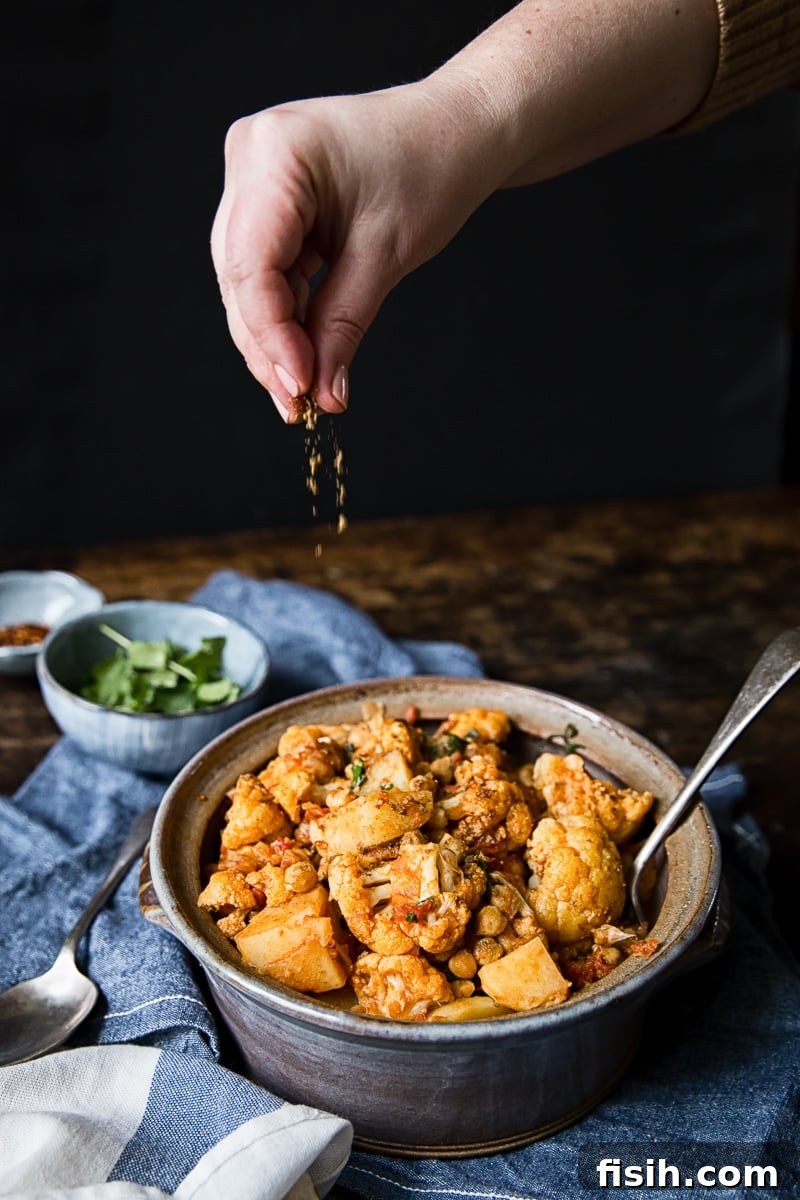 hand dropping spice onto cauliflower and potato curry