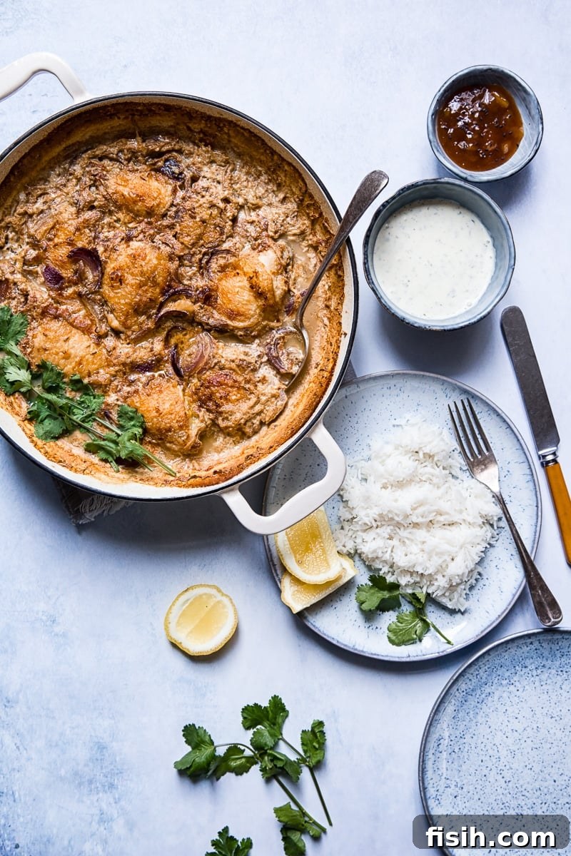 Spiced Chicken Thighs Braised in Milk in a pan next to a plate of rice and extra sauces