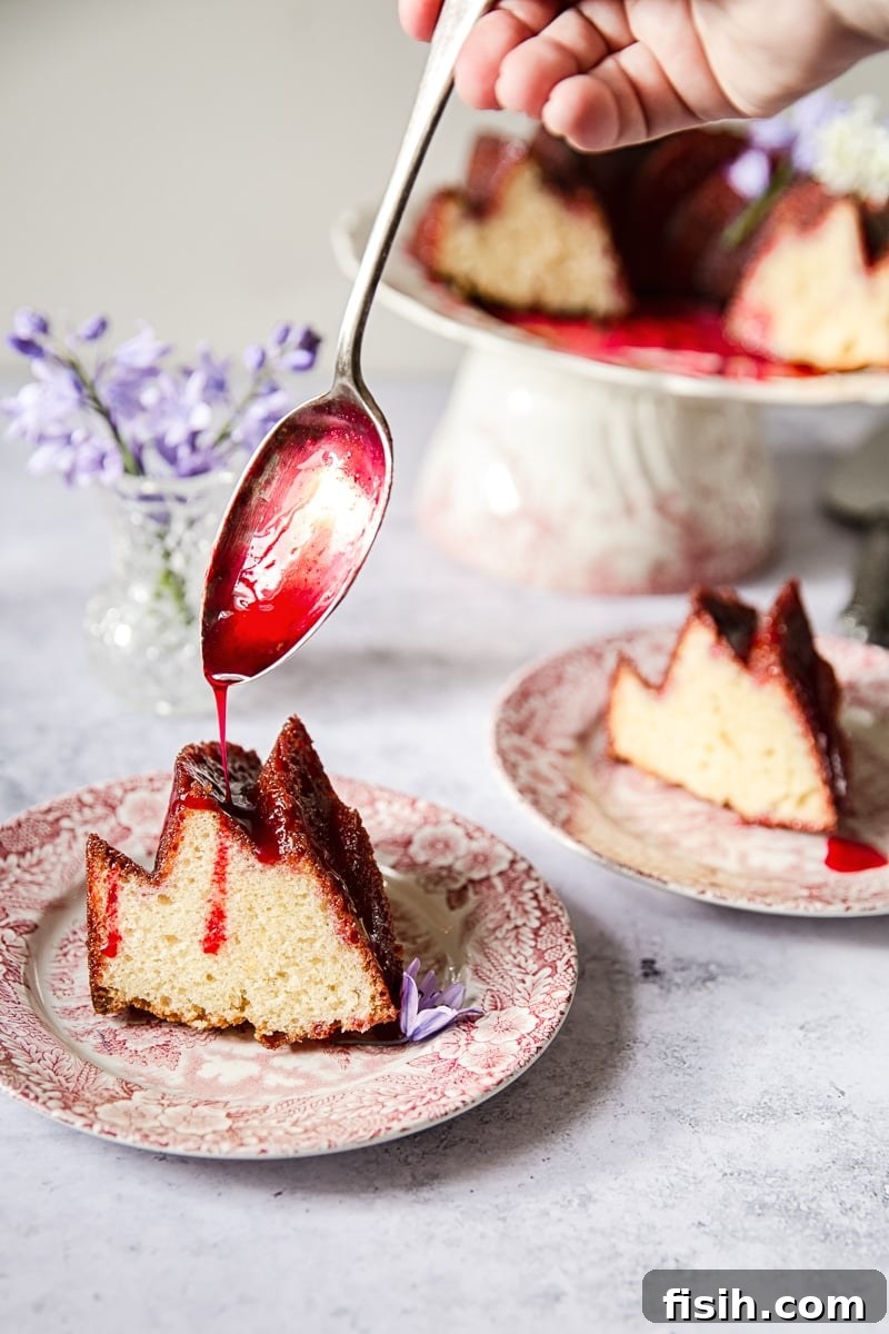 A beautifully sliced Lemon Ricotta Cake showing its moist, golden crumb contrasting with the deep red blackberry glaze, garnished with fresh berries.