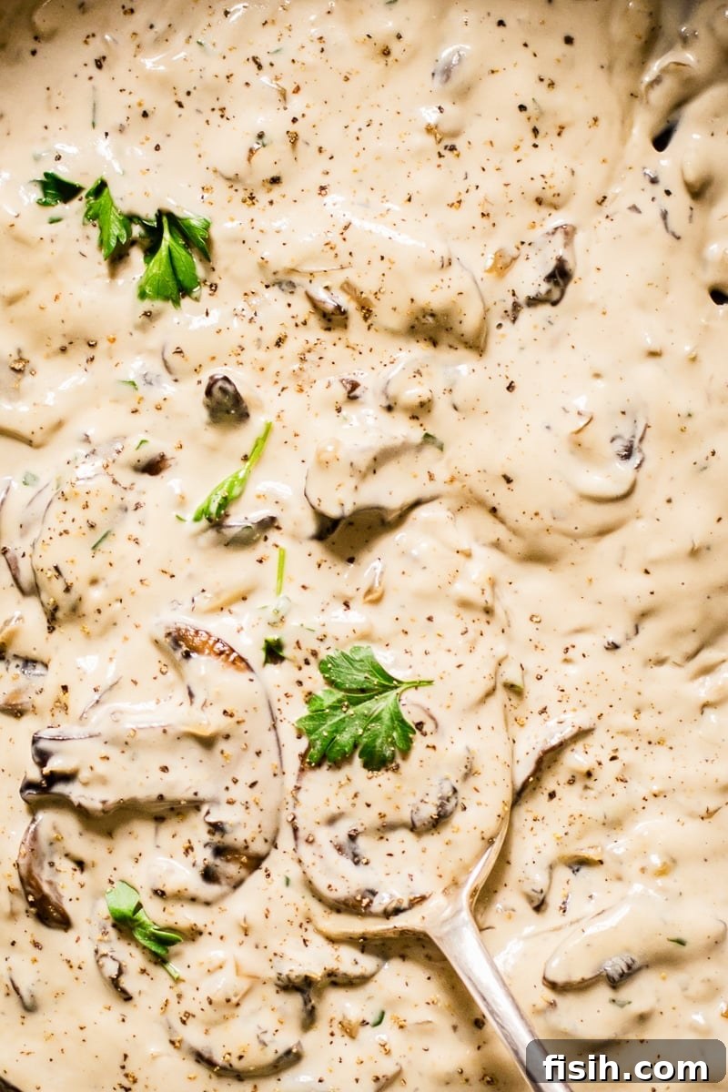 Close up of sliced mushrooms and fresh parsley infused in a creamy cognac sauce, ready for seasoning