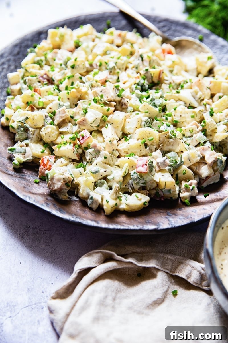 Side view of a generous serving of Russian potato salad (Olivier) on a rustic brown platter, ready to be enjoyed.