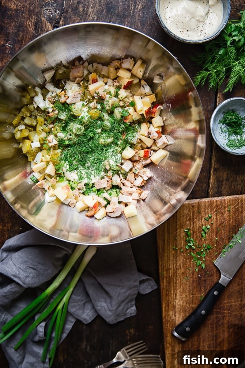 Undressed Russian potato salad ingredients, diced and ready for mixing, in a sleek stainless steel bowl, highlighting the fresh components before the dressing is added.
