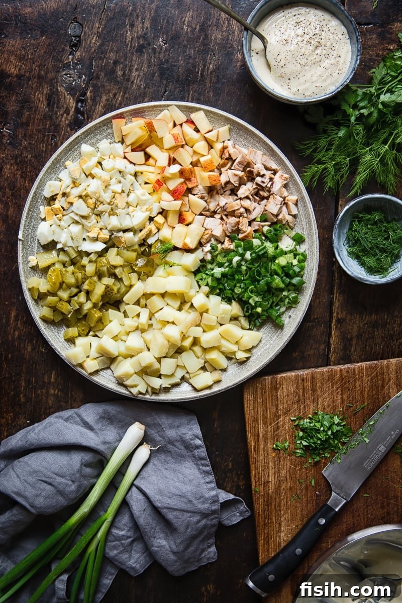 A vibrant display of Russian salad Olivier ingredients laid out on a platter, including diced vegetables, green onions, fresh herbs, and a bowl of creamy dressing, with a cutting board in the background.