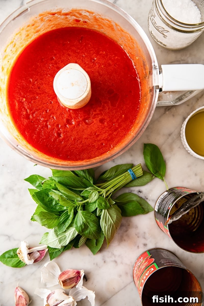 Food processor full of red sauce next to fresh basil and empty cans