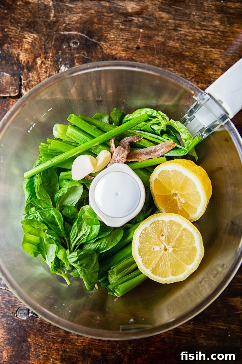 A food processor filled with fresh green herbs and bright lemons, ready to make dressing.