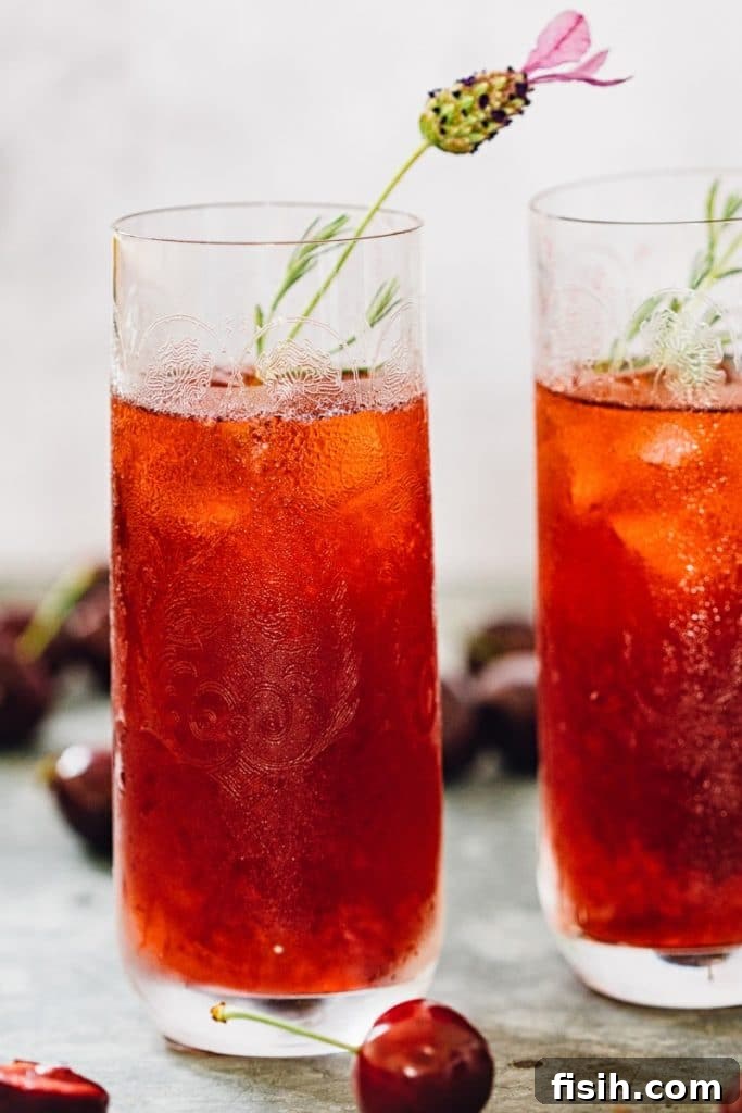 Two tall glasses filled with refreshing Cherry Long Island Iced Tea, garnished with fresh cherries and a sprig of lavender, set against a summer backdrop.