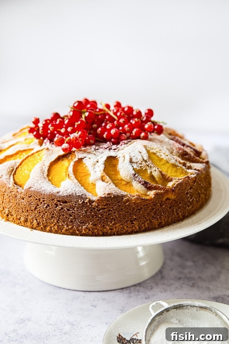 Beautifully baked peach cake on an elegant cake stand, showcasing fresh peaches and red berries