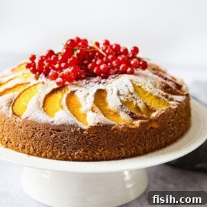 A vibrant summer peach cake with red berries on a cake stand, ready to be served