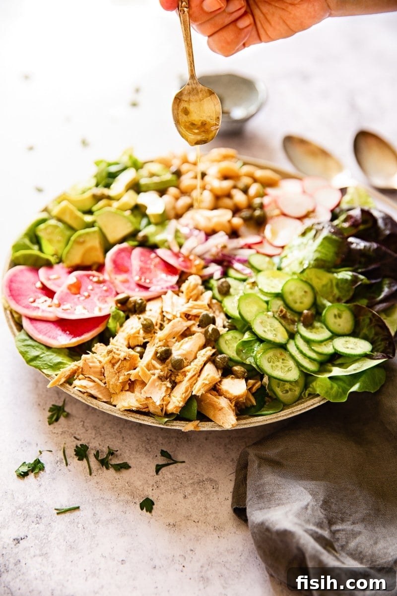 A close-up of healthy tuna salad being drizzled with a rich vinaigrette from a spoon