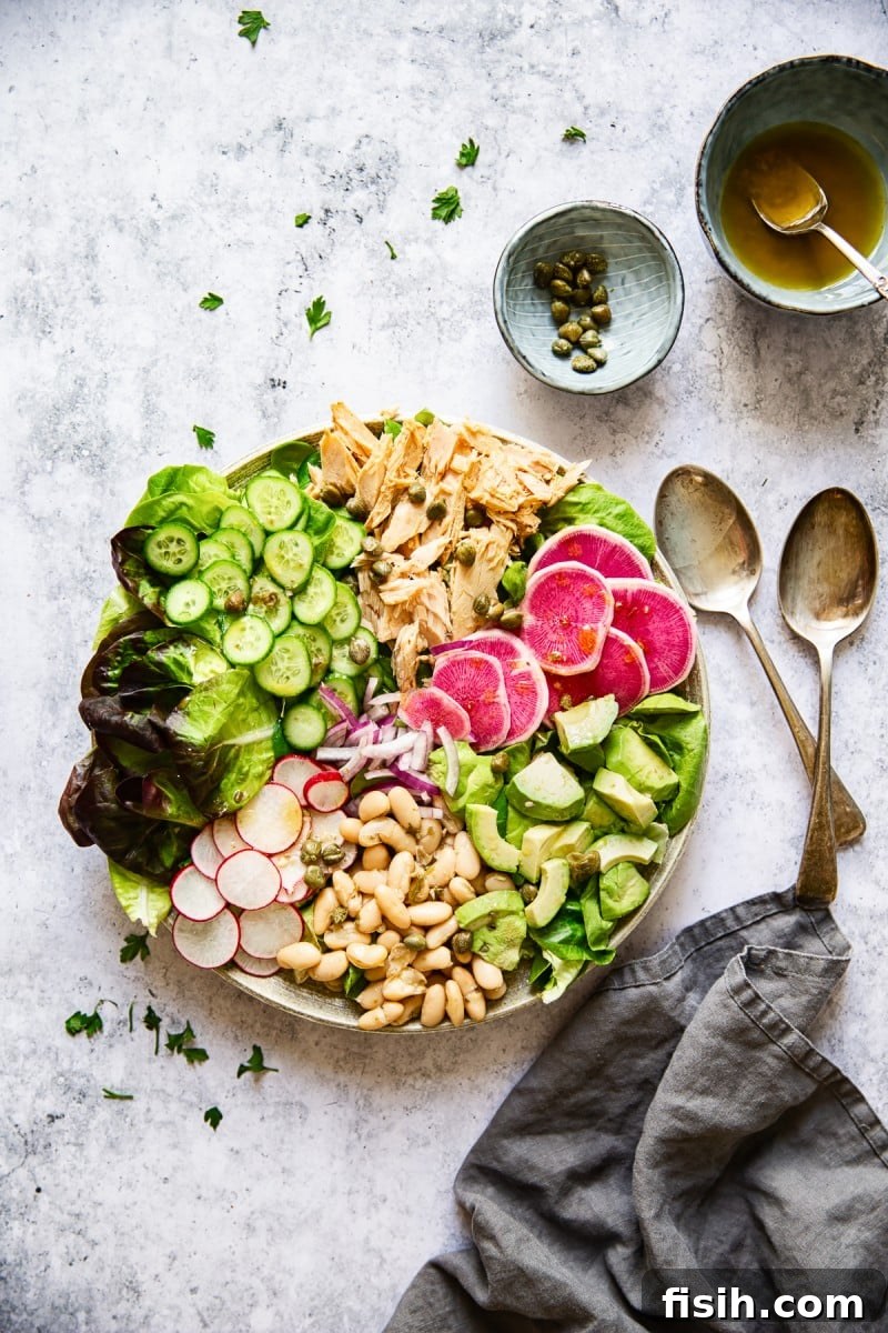 Overhead shot of a bowl of healthy tuna salad, surrounded by small bowls of ingredients like capers and dressing