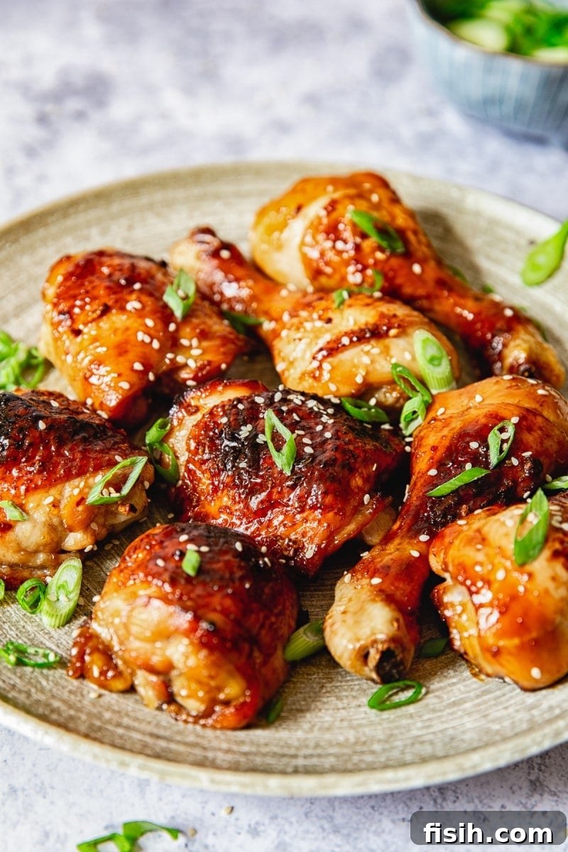 Side view of glossy, sticky Asian chicken thighs and legs on a elegant platter, garnished with fresh herbs.