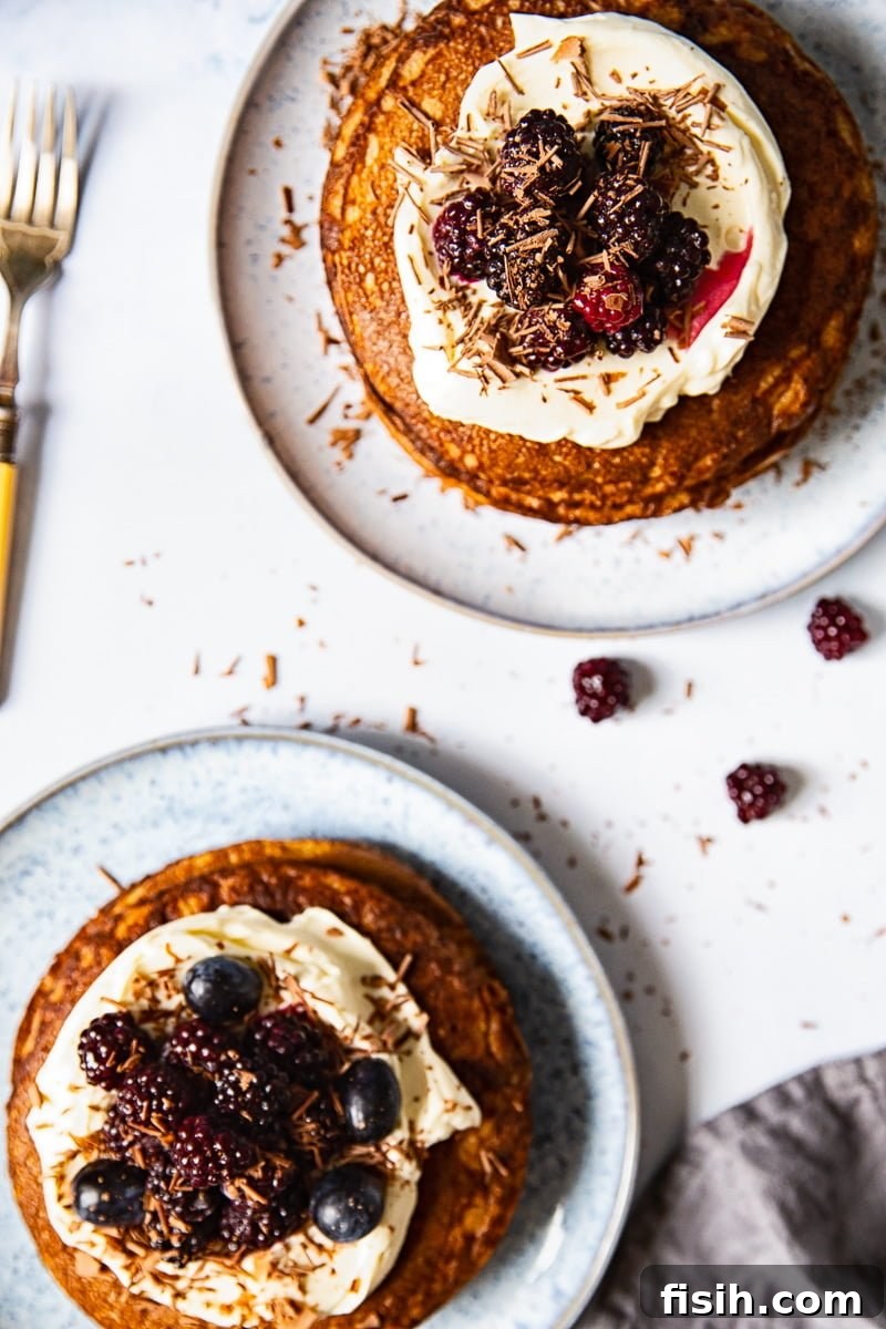 A top-down view of two blue plates, each holding a stack of fluffy buckwheat pancakes, adorned with fresh whipped cream and a sprinkle of vibrant berries, accompanied by a fork ready for enjoyment.