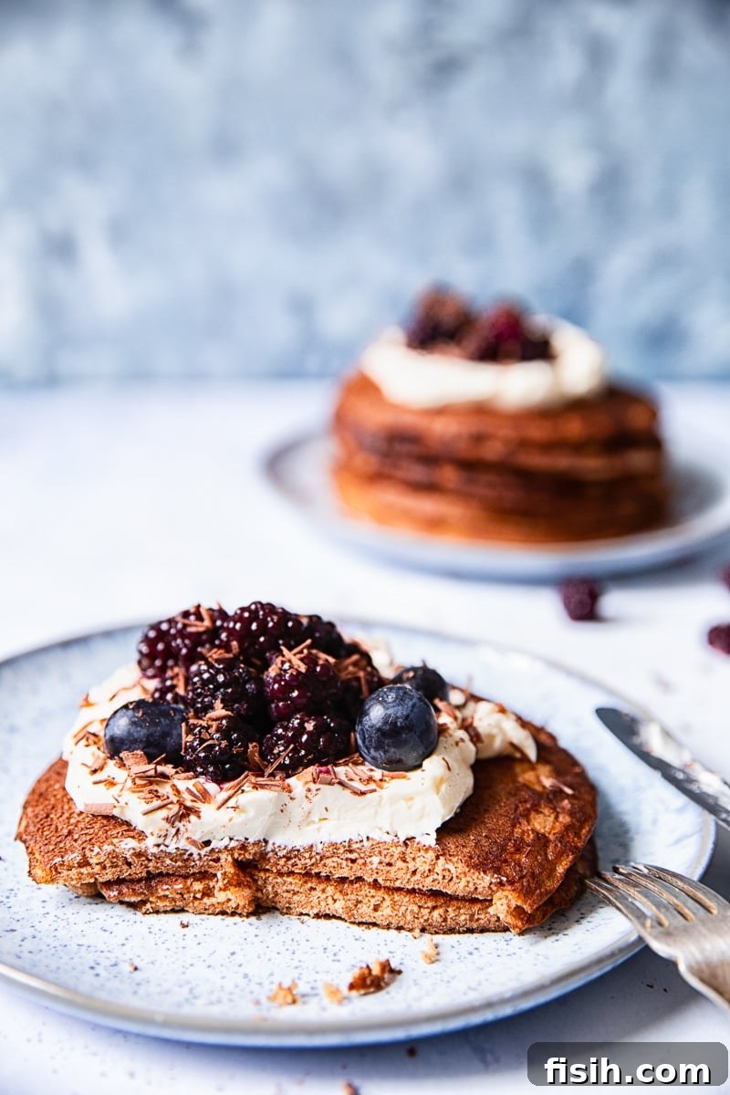 Two golden buckwheat pancakes presented on a light blue plate, with a portion delicately cut off, while another plate bearing more pancakes waits invitingly in the soft-focus background.