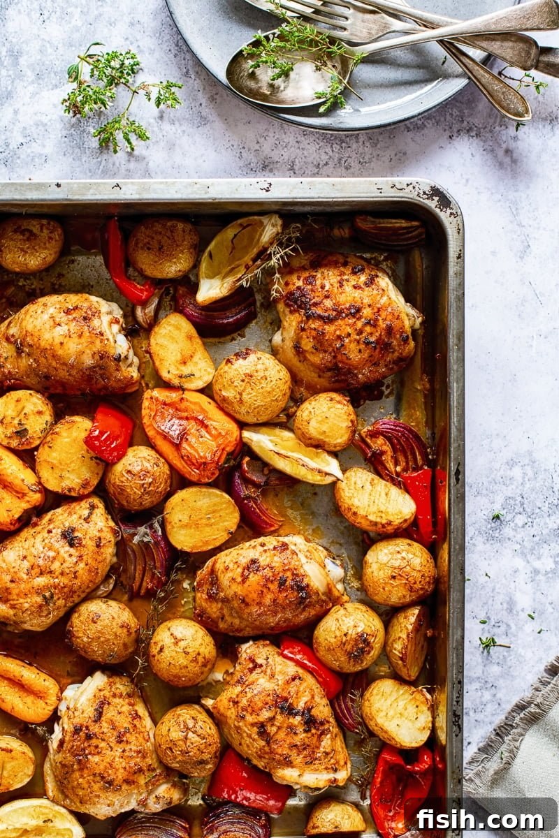 Top-down view of a corner of a baking tray filled with seasoned chicken, potatoes, and peppers before baking