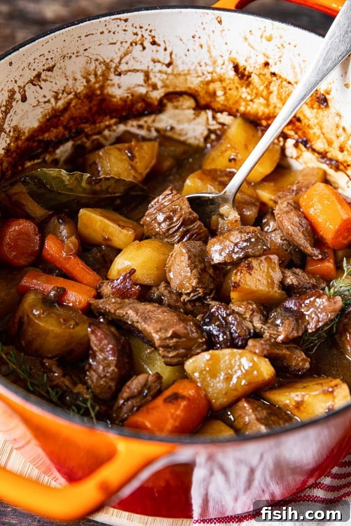 Close-up of a rustic orange Dutch oven filled with bubbling Irish Beef Stew, showcasing its rich texture.