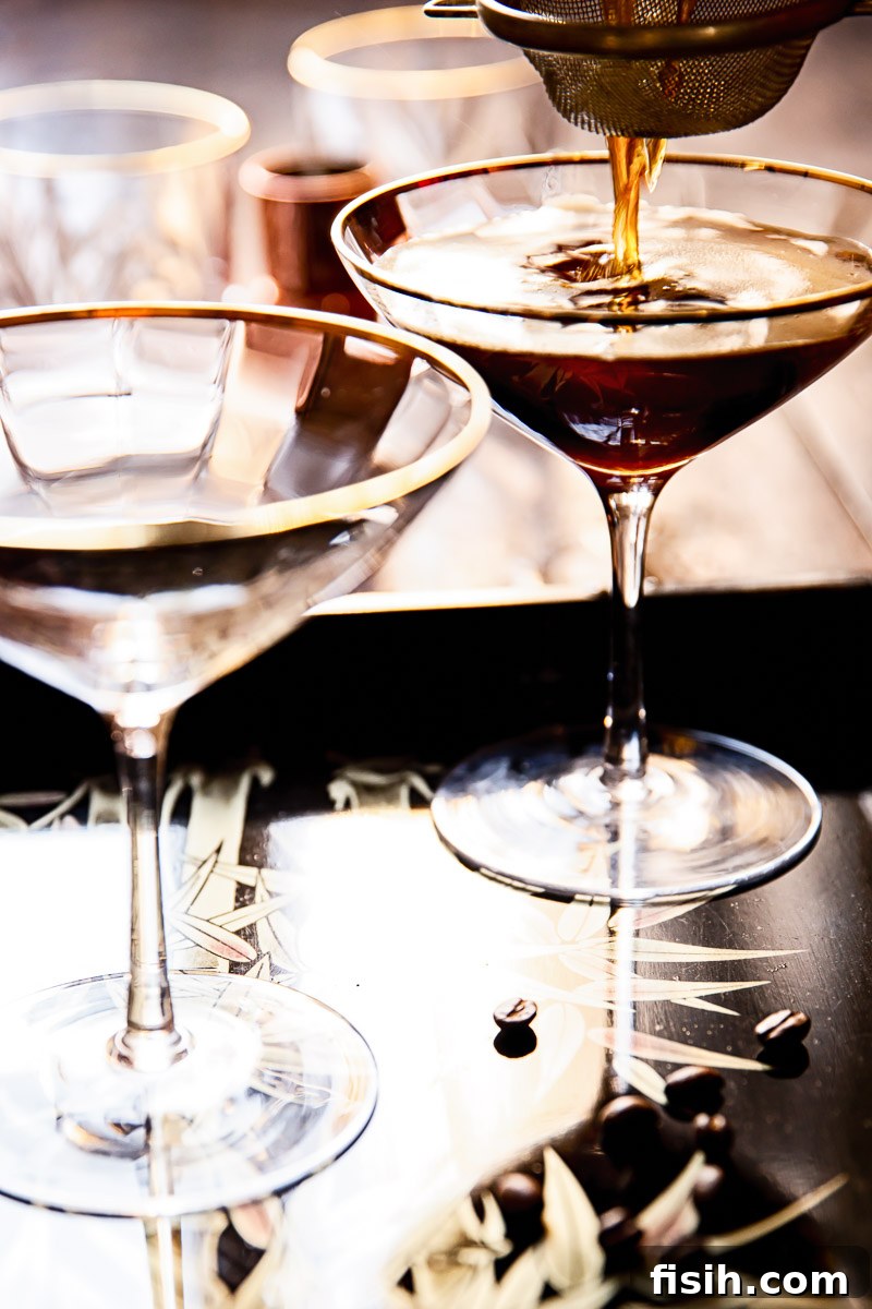 Espresso Martinis being poured from a cocktail shaker through a strainer into glasses.