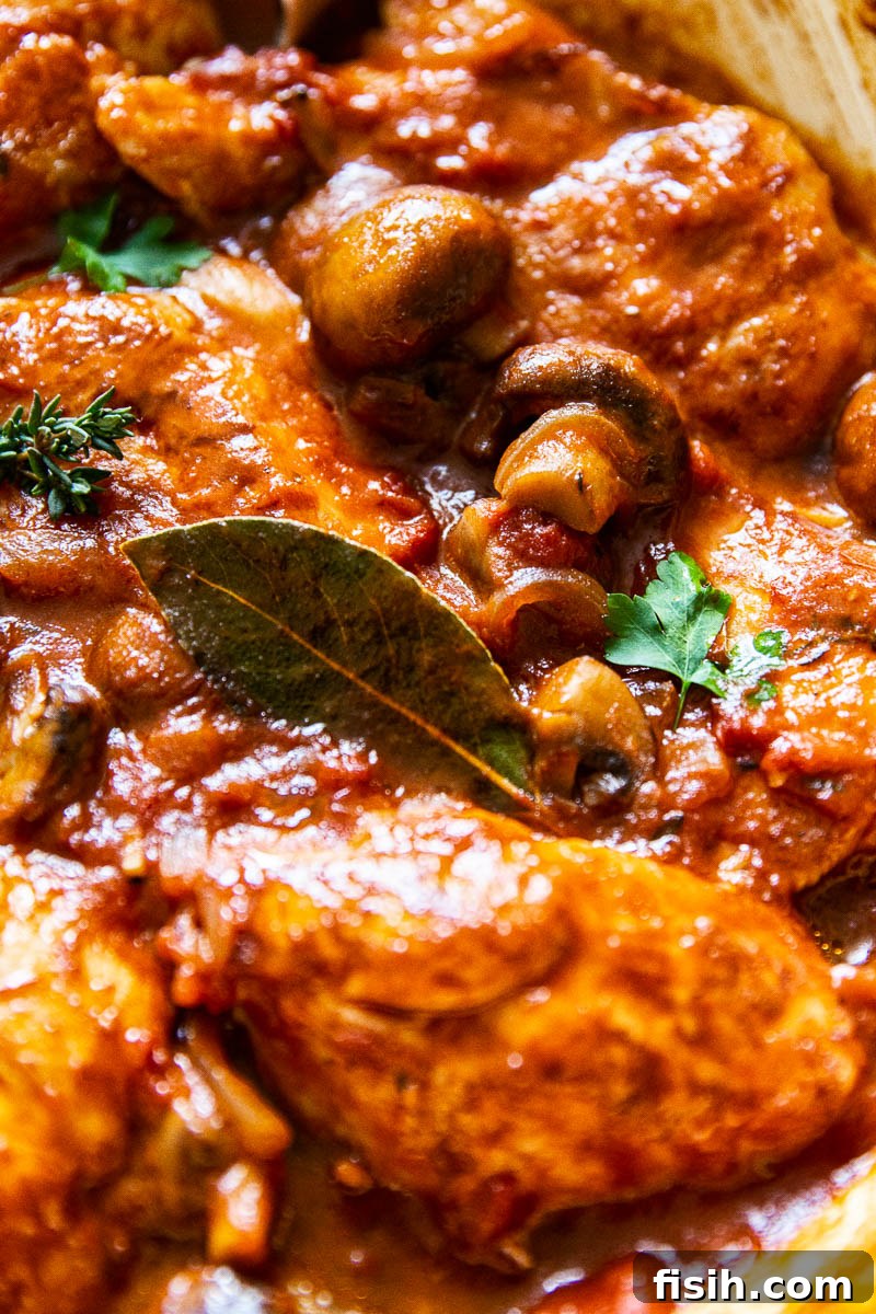 A close-up view of Chicken Chasseur in a pan, with a prominent bay leaf, highlighting the rich texture of the sauce and tender chicken.