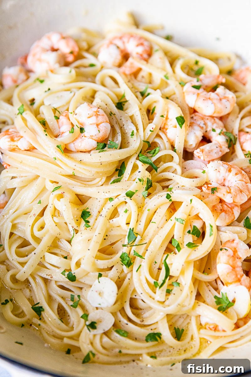 Close-up view of Shrimp Scampi Linguine in a white bowl, showcasing the glistening sauce, perfectly cooked shrimp, and fresh parsley garnish.