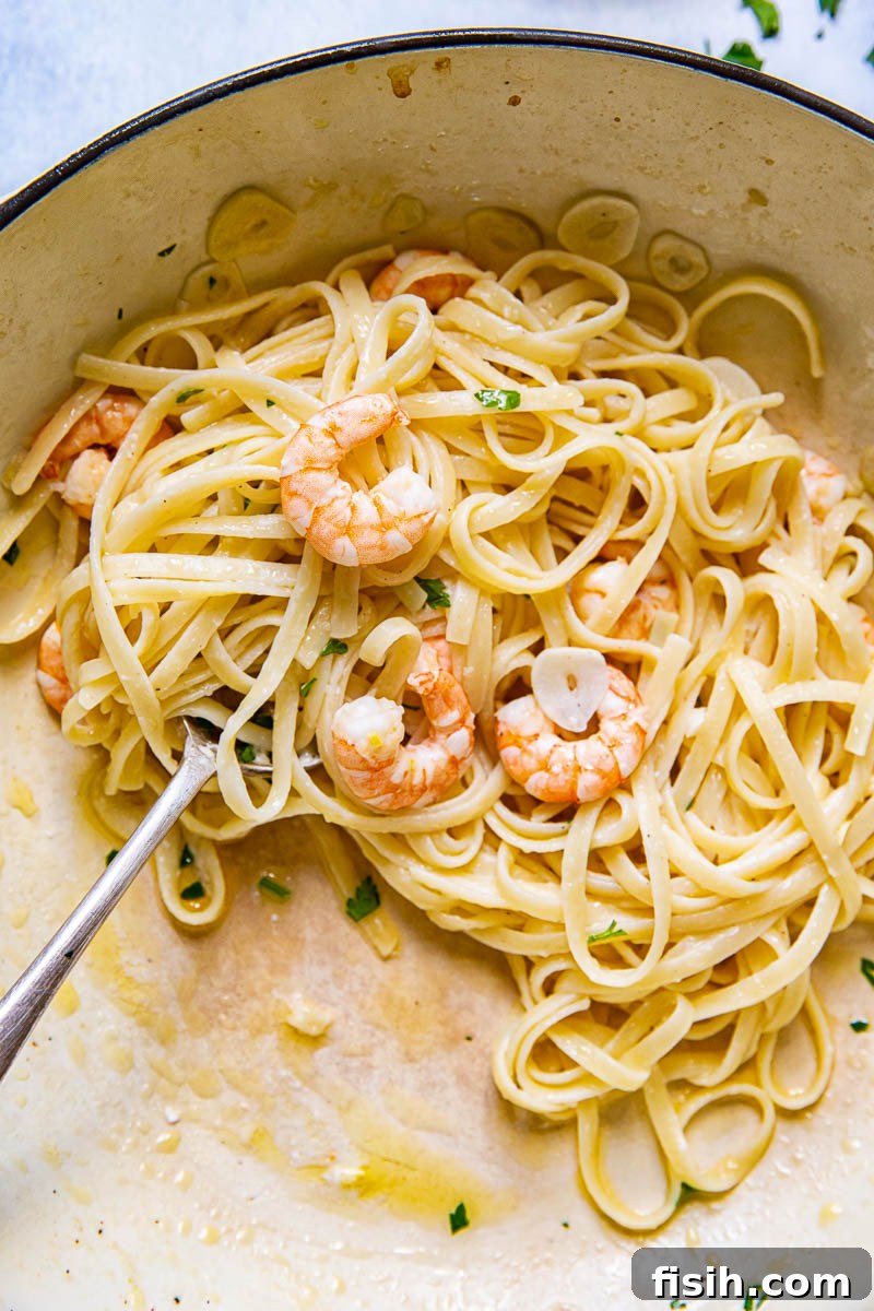 Overhead shot of Shrimp Scampi Linguine simmering in a large cast iron pan, showing the rich sauce, pasta, and shrimp ready to be served.