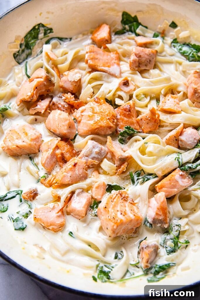 Close-up of salmon pasta in cream sauce with greens, garnished with fresh herbs.