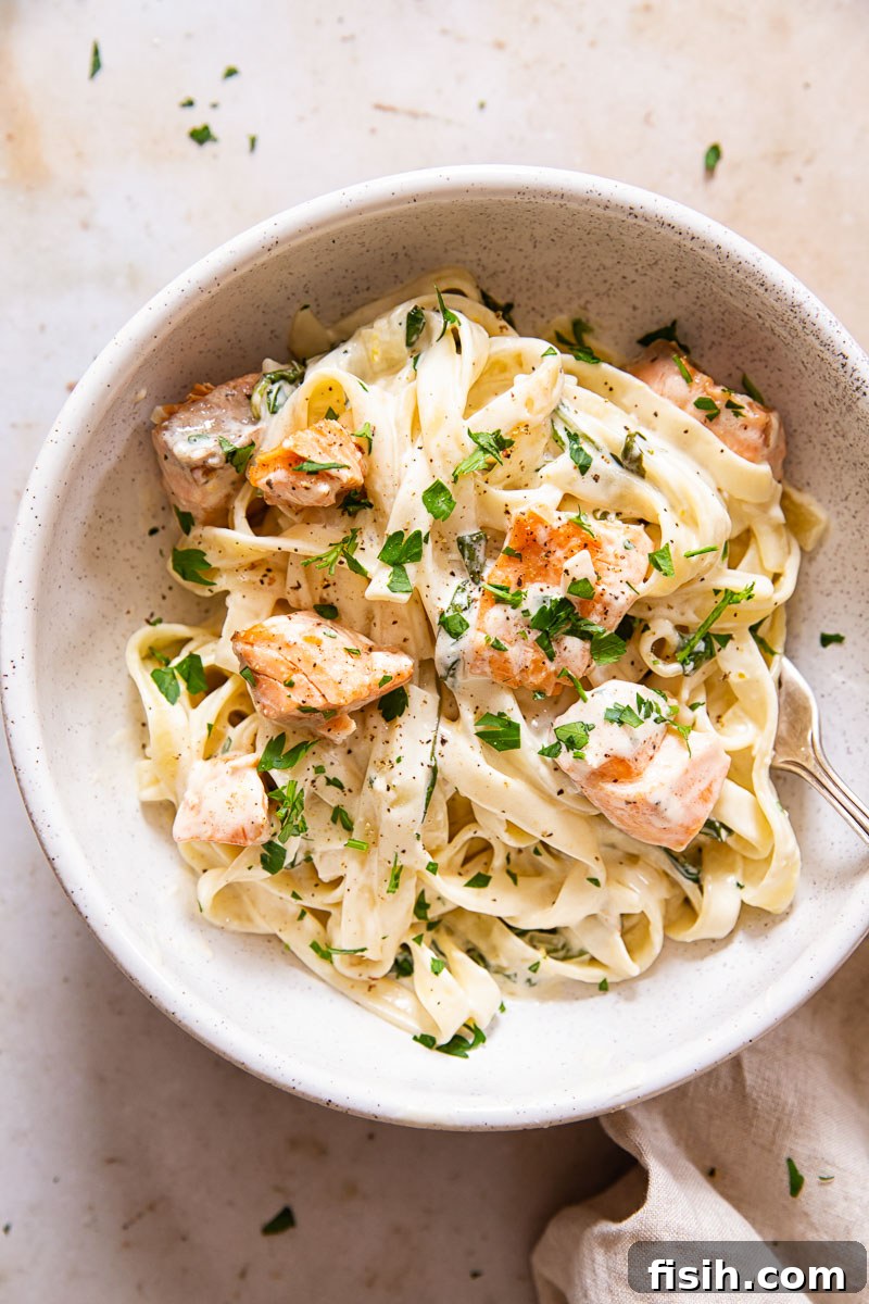 A serving of creamy salmon pasta in a bowl, garnished with fresh herbs and a lemon wedge.